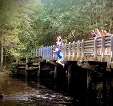 a group of people jumping off a bridge into the water