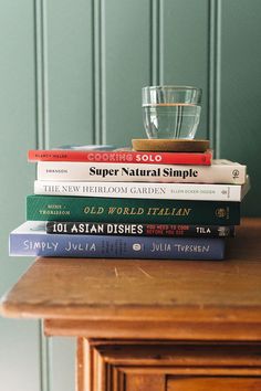 a stack of books sitting on top of a wooden table next to a glass cup