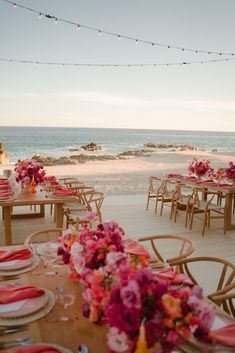 tables set up on the beach with pink flowers in vases and place settings for dinner