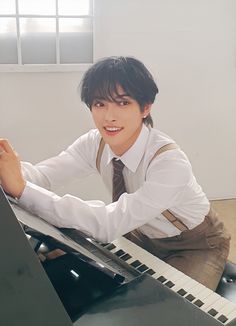 a young man sitting at a piano with his hands on the keyboard and looking into the camera