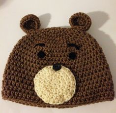 a crocheted brown bear hat with black eyes and nose is on a white surface