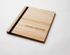 a wooden notebook with writing on the front and bottom, sitting on a white surface