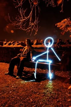 a man sitting on top of a bench next to a tree with light painted on it