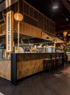 the inside of a restaurant with wooden tables and stools in front of an open air kitchen