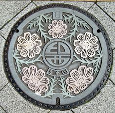 a manhole cover on the ground with flowers and symbols painted on it's sides