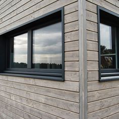 two windows on the side of a house with wood siding and black trim around them