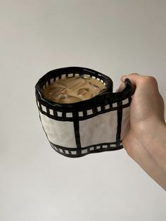 a hand holding a black and white cup with liquid in it's bottom compartment