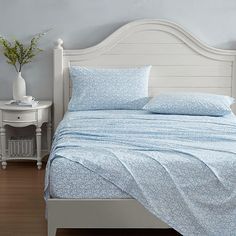 a bed with blue sheets and pillows in a bedroom next to a white nightstand table