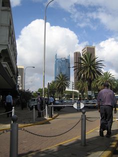 a man is walking down the sidewalk in front of some tall buildings and palm trees