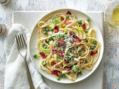 a white plate topped with pasta and peas next to a glass of wine on top of a table