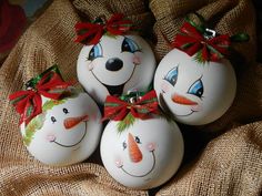 four snowman ornaments with red bows are sitting on a burlap cloth covered surface