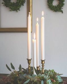 four candles are lit on a table with succulents and greenery