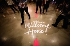 a group of people standing around with the words you are welcome here written on the floor