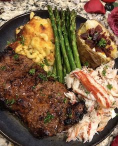 a black plate topped with meat, potatoes and asparagus next to a baked potato