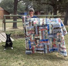 a woman standing next to a quilt on top of a grass covered field with a black and white dog sitting in front of it