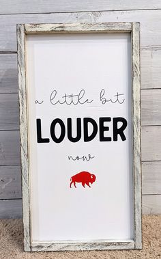 a little but louder now sign in a frame on the floor next to a wall