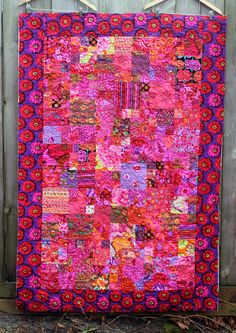 a pink and purple quilt hanging on a wooden fence