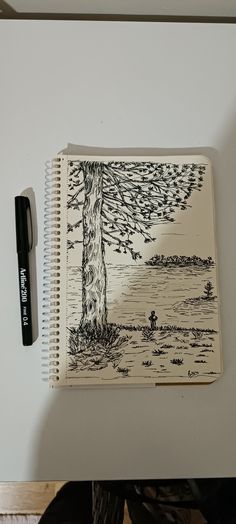 an open notebook with a drawing of a tree on it next to a black pen