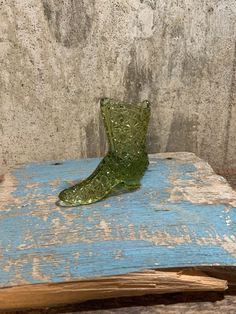 an old book with a glass boot on it sitting on a wooden table next to a concrete wall