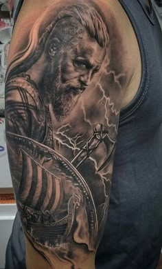 a man's arm with a black and grey tattoo on it, featuring a viking warrior