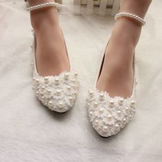 a pair of white shoes with pearls on the heel and ankle straps, sitting on a bed