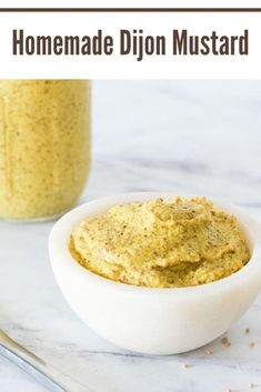 homemade dijon mustard in a small white bowl on a marble counter with a jar behind it