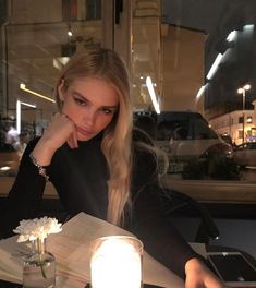 a woman sitting at a table with a book in front of her and a candle