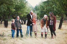 a group of people standing around each other in the grass with trees and bushes behind them