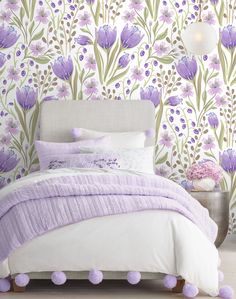 a bed sitting next to a wall with purple flowers painted on it and pom poms