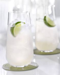 two glasses filled with ice and limes on a table