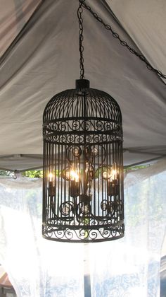 a birdcage hanging from the ceiling in front of a window with white curtains