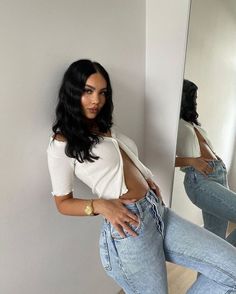 a woman in jeans leaning against a wall with her hands on her hips and looking at the camera