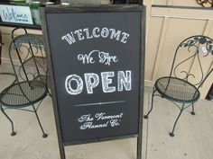 a sign that says welcome to we are open and two chairs sitting in front of it