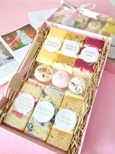 a pink box filled with lots of different types of cakes and pastries on top of a table