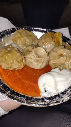 a person holding a plate with dumplings and sauce on it