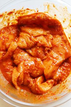 a bowl filled with meat and sauce on top of a white countertop next to a wooden spoon