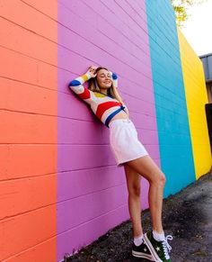 a woman leaning against a colorful wall with her hands on her head and arms behind her head