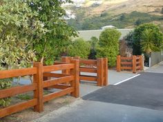 a wooden gate is in front of some bushes and trees on the side of a road