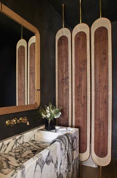 a bathroom with black walls and marble counter tops, gold trimming on the mirror