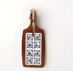 a wooden cutting board with blue and white tiles on it, hanging from a hook