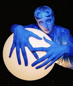 a man with blue hands on top of a white ball in the dark night sky