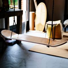 a wooden skateboard sitting on top of a floor next to a chair and table