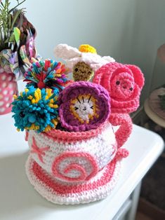 a crocheted basket with flowers in it sitting on a white table next to a potted plant