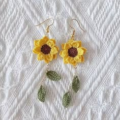 two yellow crocheted flowers with leaves hanging from them on a white surface,