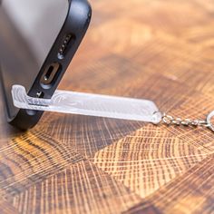 a cell phone is being held up by a keychain on a wooden table