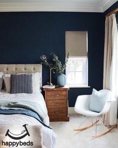 a bedroom with blue walls and white bedding, rocking chair in the foreground