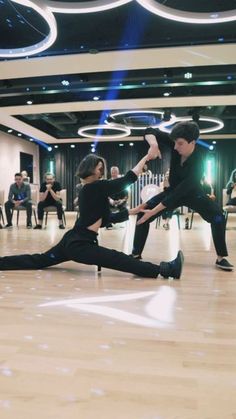 two young men are dancing on the dance floor while others sit in chairs behind them