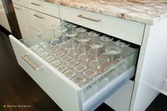 an open drawer with wine glasses in it on a counter top next to cabinets and drawers