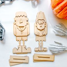 two wooden cutouts of people standing next to each other on a table with pumpkins