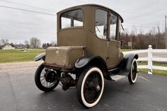 an old car is parked on the side of the road in front of a white fence